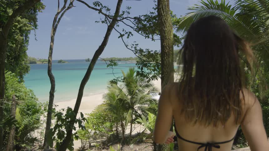 A woman in a swimsuit walks towards the beach