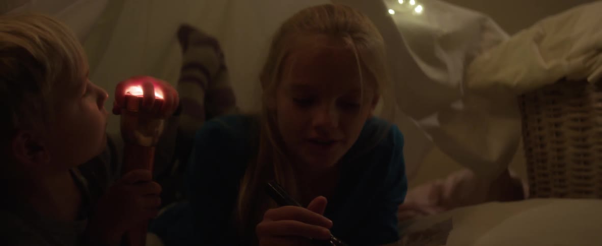 Young boy holds a flashlight while laying on a bed with his older sister who is holding a paper and a marker