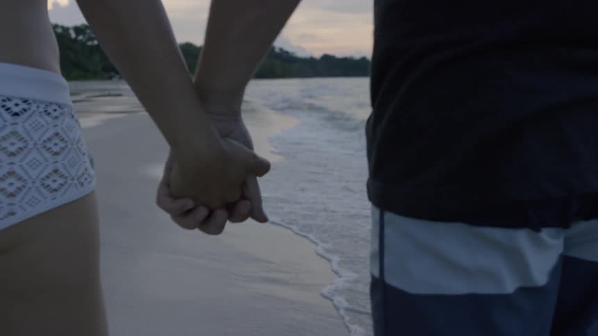 A man and woman hold hands on a beach at sunset
