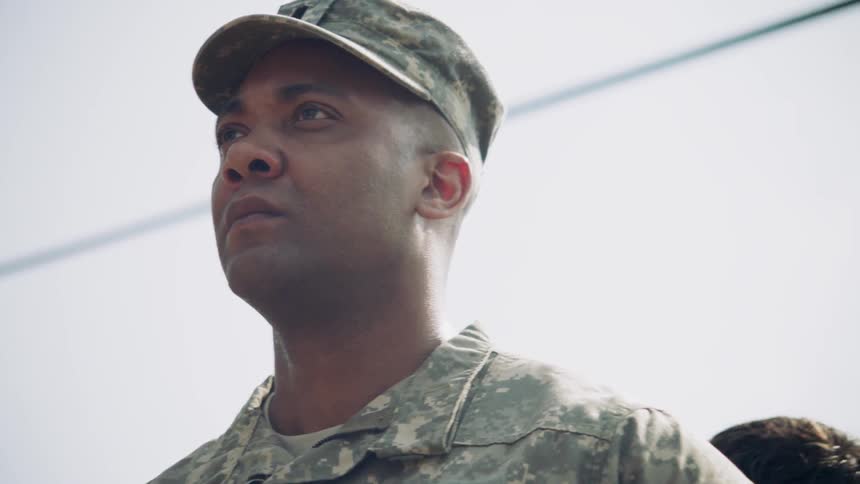 A man in a military camouflage uniform stands outside
