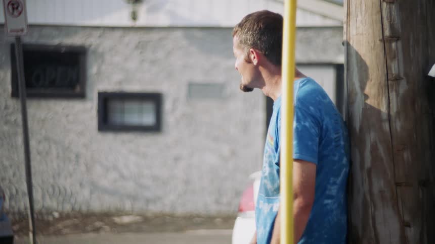 The man leans against the pole smoking a cigarette