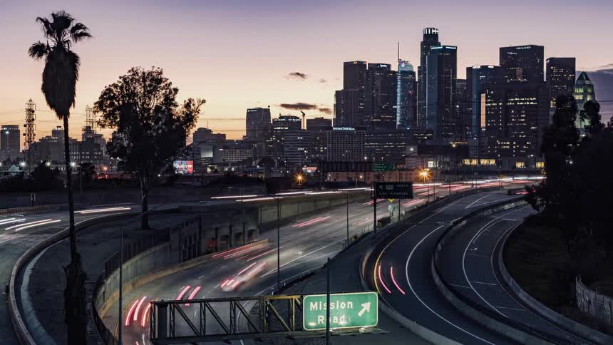 Wind blows the trees as cars travel on a city highway