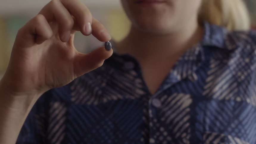 A woman looks at small purple objects in her hand
