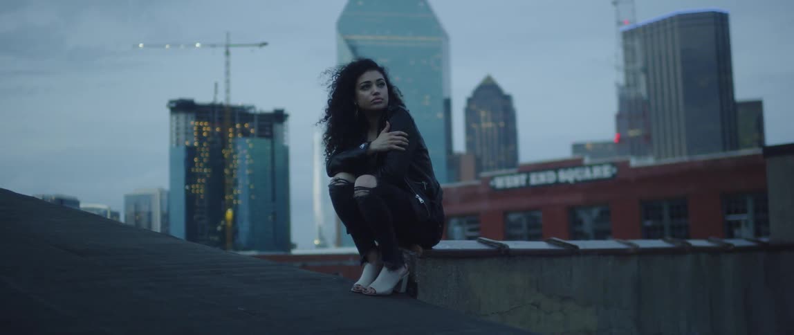 A woman is sitting on top of a roof with the city behind her