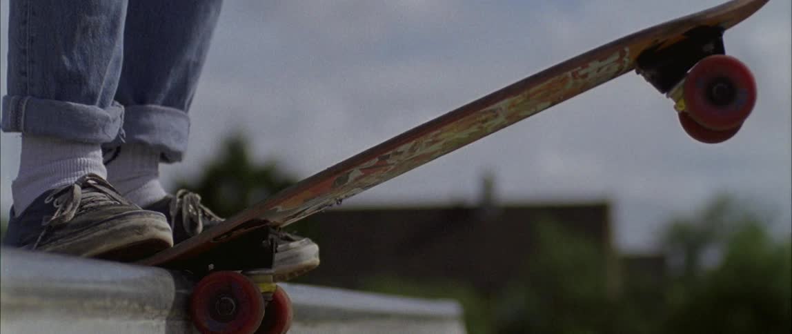 A skateboarder stands on a ledge in a skate park