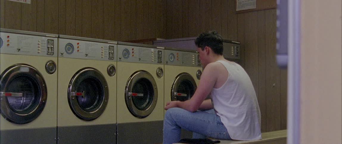 A man is sitting in a laundromat watching a dryer spin during the day