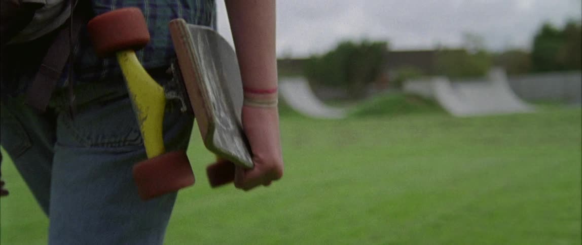 A teenager carries a skateboard towards a skatepark