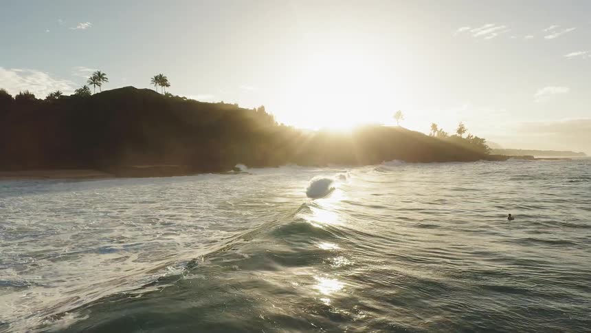 The surfer floats over the wave at sunrise