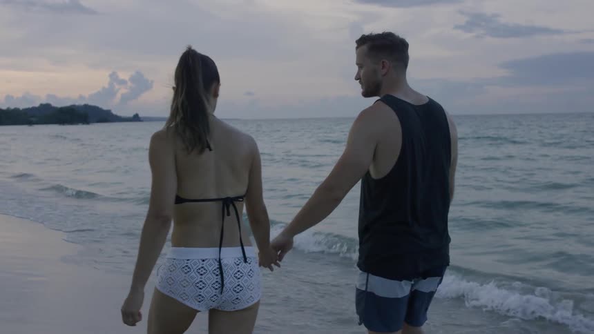 A couple holds hands as they walk on the beach at sunset