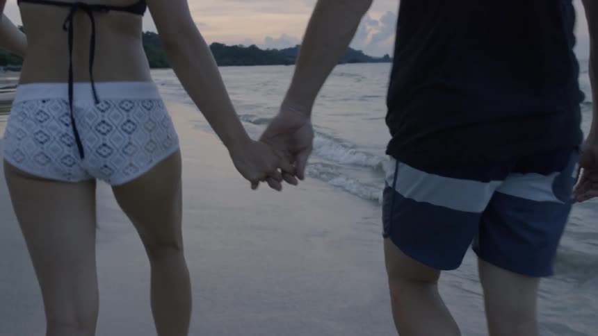 A man and woman walk on the beach while holding hands