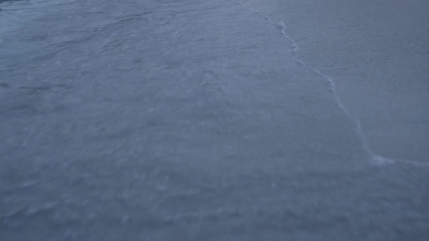 Waves are crashing and rolling onto a beach at dusk