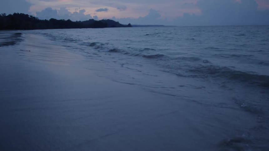 Small waves are crashing on the beach at sunset