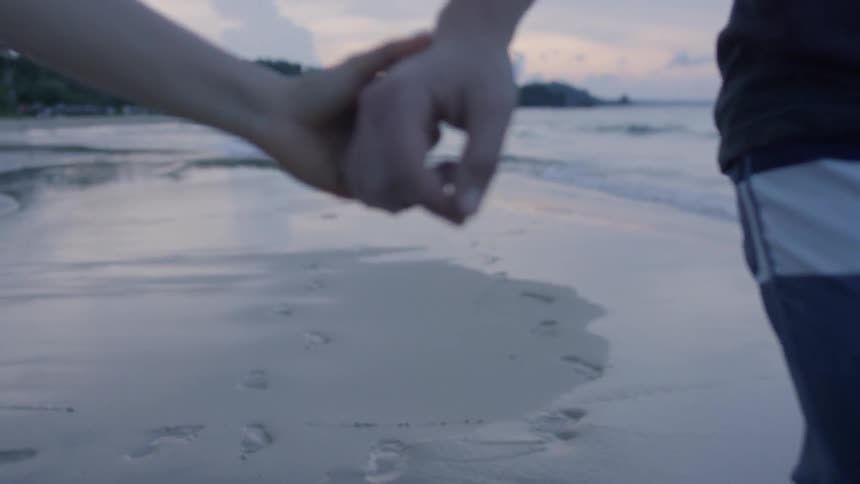 A man and woman hold hands on the beach