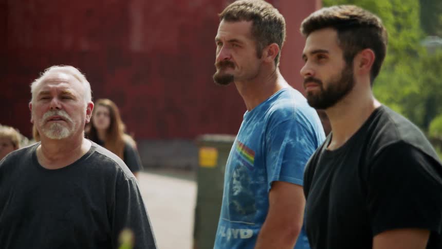 A group of men are standing outside watching an event unfold in daylight
