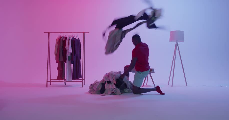 Man runs towards a pile of clothing and scatters it around the room