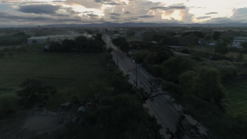 A vehicle travels on a rural road on a cloudy day