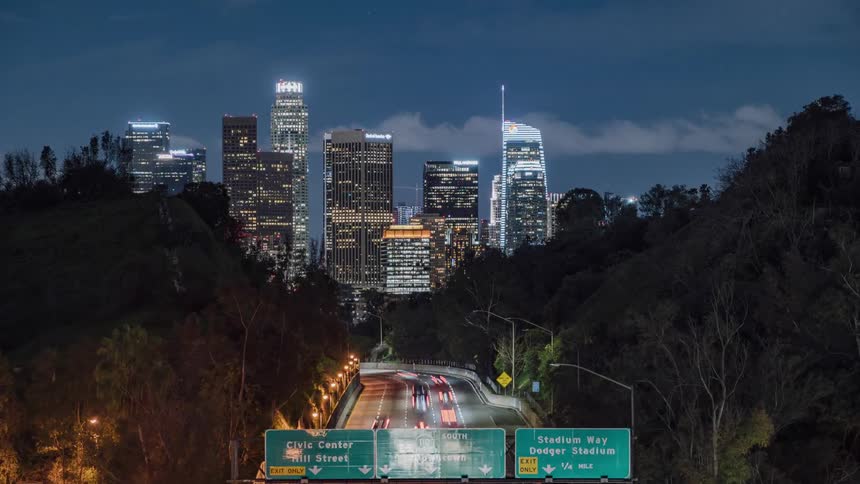 Vehicles drive on a busy highway towards a city at night