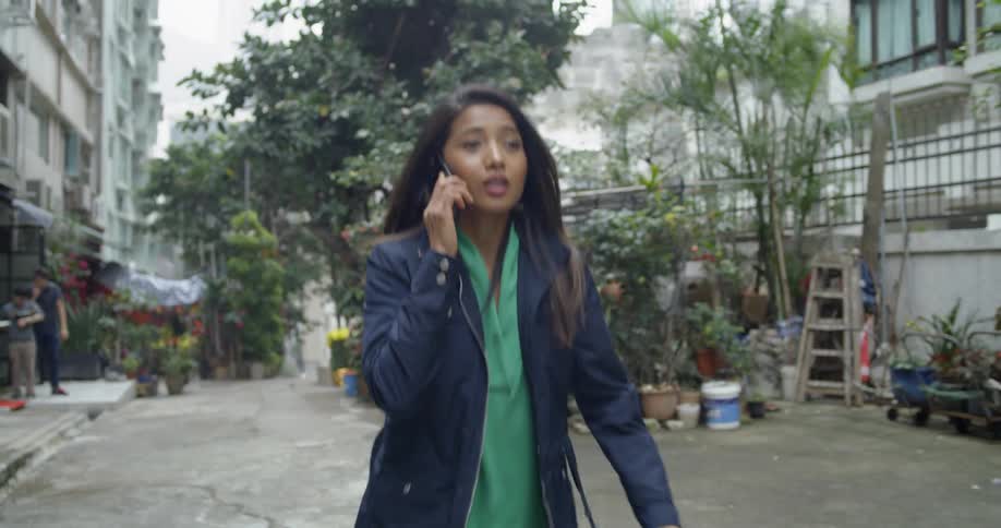 A woman is talking on her cell phone as she walks through a garden center in a city