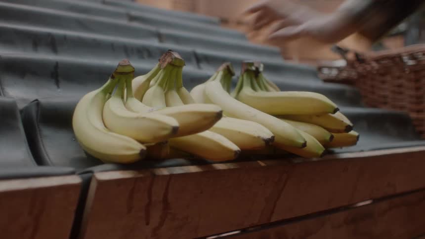 A person is putting bunches of bananas into a market stall during the day