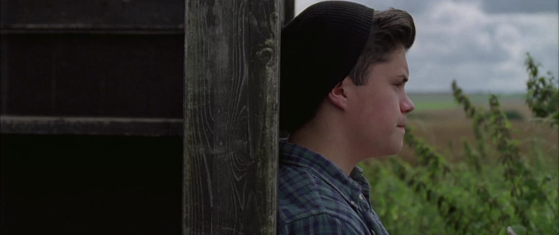 A young man leans against an old wooden structure