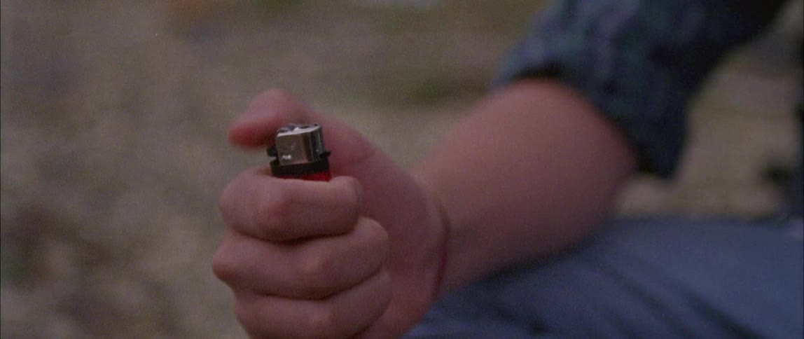 A teenager plays with a lighter while sitting on the ground