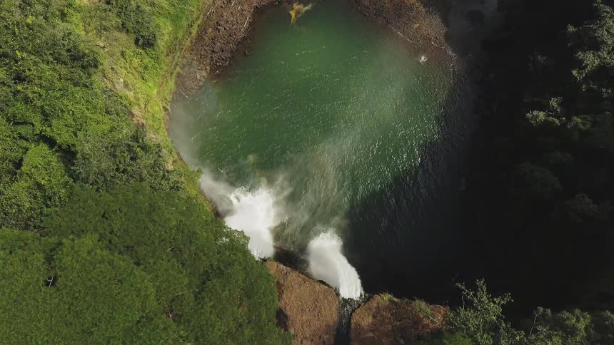 Waterfalls are cascading over a cliff into a lagoon on a sunny day