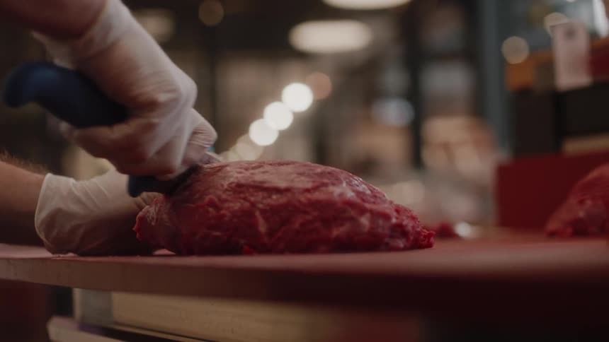 A person is cutting a big piece of red meat