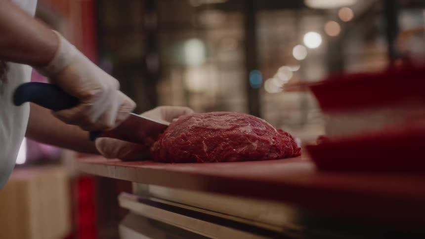 A butcher is cutting a large piece of meat