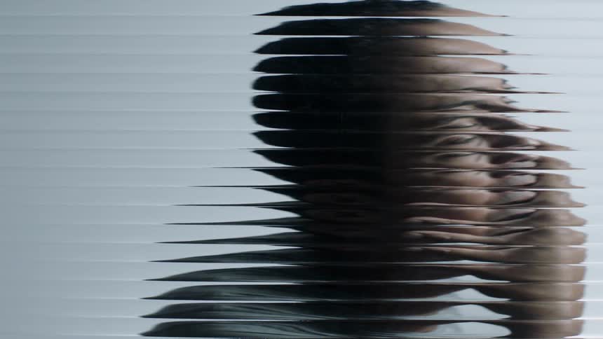 A person rubs their face behind the blurry glass