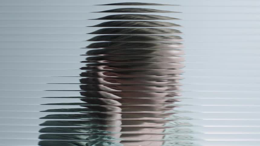 A woman sits behind a textured window