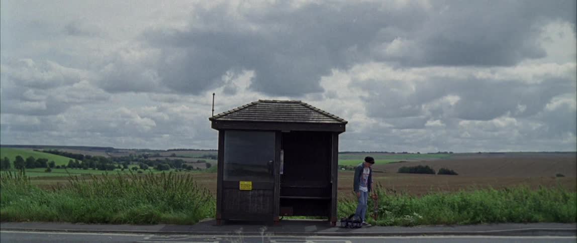 A teenager sits on the ground next to a bus stop