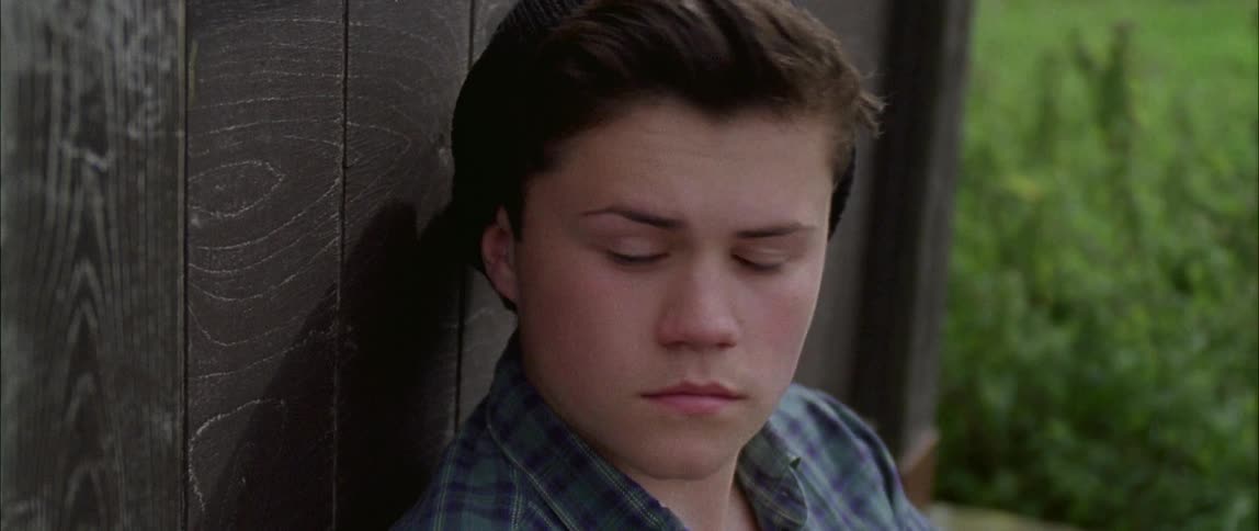 A boy sits against the shed before getting up