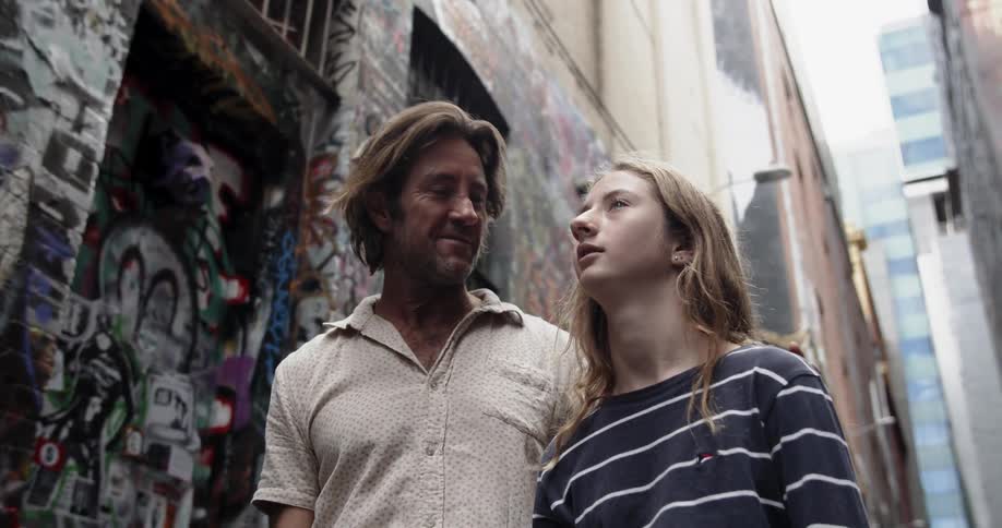 A man talks to a young girl in a graffiti covered alley