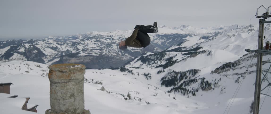 A man does a backflip in snowy mountains