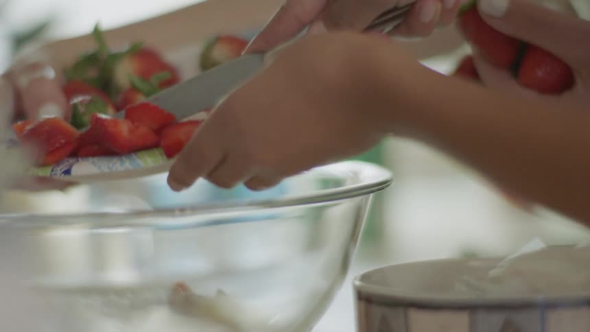 Cut strawberries are pushed into a glass bowl