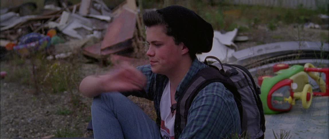 A skateboarder sits in the gravel and throws pebbles