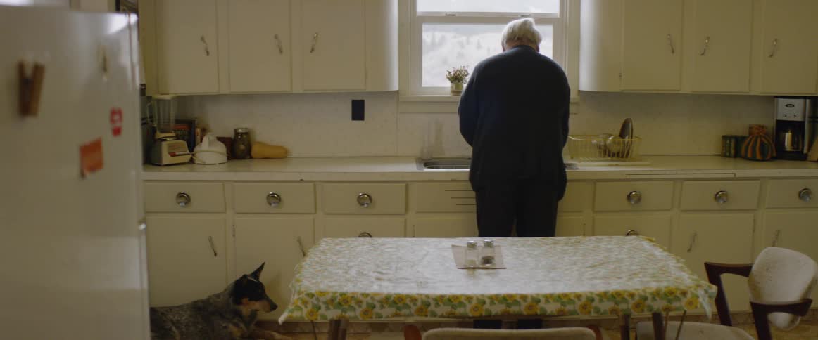 An old man is washing up his bowl in a kitchen sink in daylight