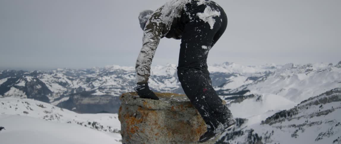 A man is lifting himself onto a pipe outside in winter in a mountainous landscape
