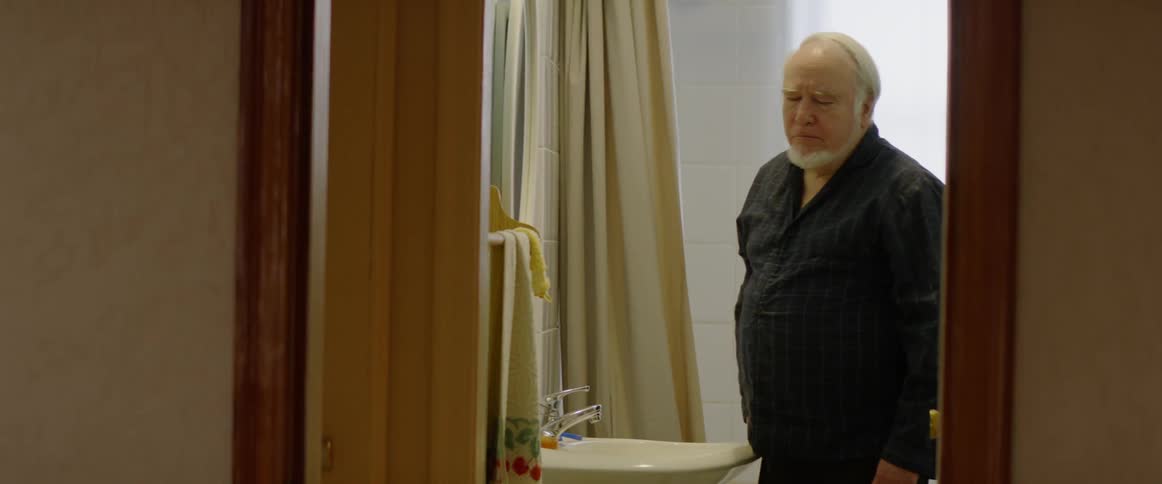 A man wipes his face with a rag then leaves the bathroom