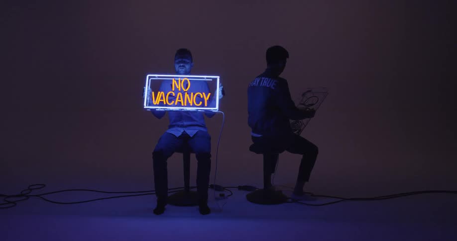 Two men hold glowing neon signs in a dark studio