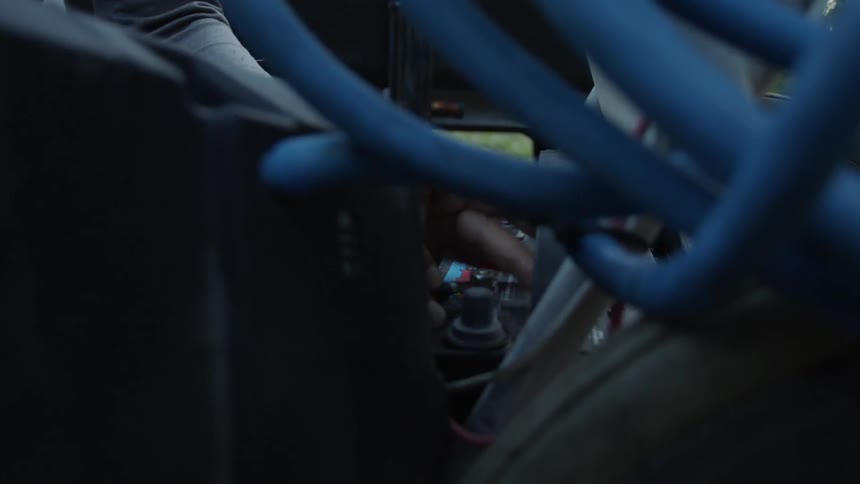 A man is tightening the screw on a vehicle battery inside in daylight