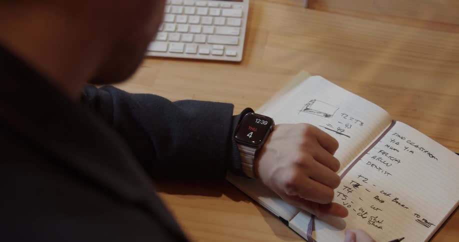 A man is checking his watch and writing in his notebook