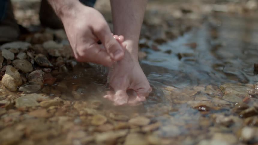 A person washes their hands in the rock filled stream