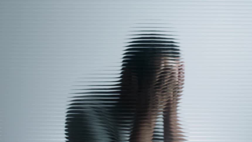 A person behind the glass holds their face