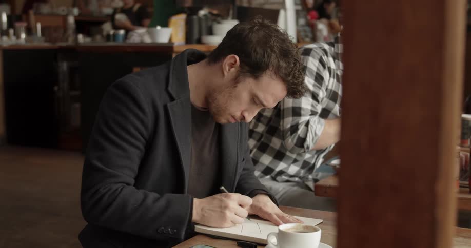 A man sitting at a table in a busy restaurant and drawing in a sketchbook