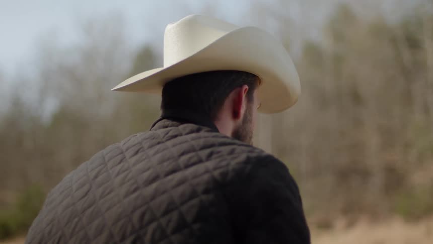 A cowboy stands outside on a ranch