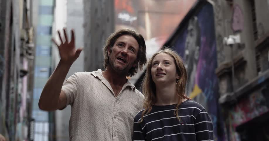 Man and teenage girl smile on a city sidewalk