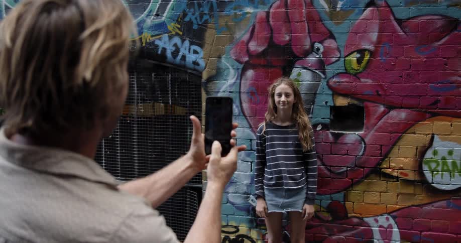 Man takes a photo of a woman standing in front of graffiti