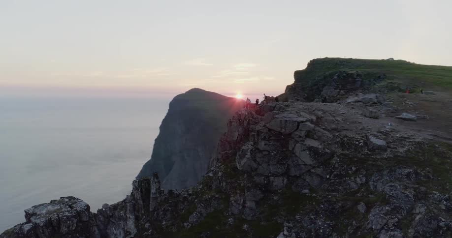 Several people stand on the edge of a cliff overlooking water