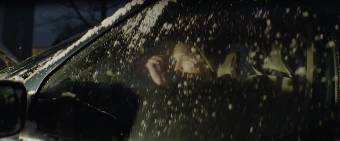 The man gets out of the car in the snow and gives a thumbs up